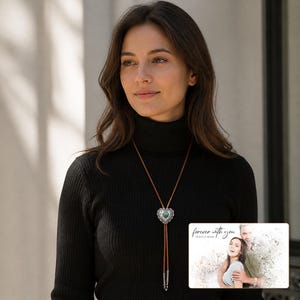 Brown cord bolo necklace with a silver-tone heart slide and turquoise-color center, worn view. A personalized greeting-card example appears in the corner.
