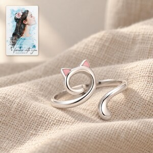 One open cat-curl ring lying on softly folded oatmeal linen. A personalized digital greeting card is shown alongside.