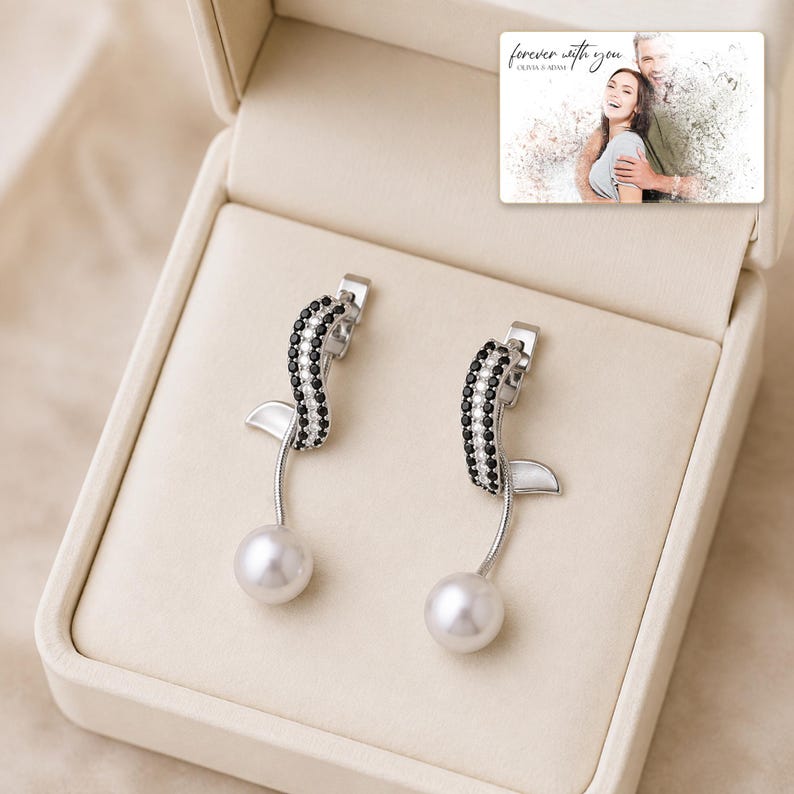 Silver-tone curved drop earrings with black accents and white round drops, presentation in an open jewelry box. A personalized greeting-card example appears in the corner.