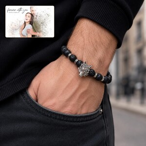 Black bead bracelet with silver-tone wolf-head detail, adult lifestyle view. A personalized greeting-card example appears in the corner.