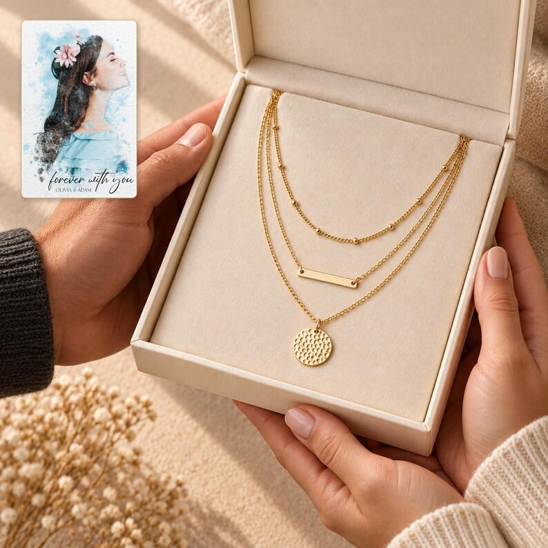 Two adults holding an open ivory jewelry box with the complete gold-tone three-layer necklace visible. A personalized digital greeting card is shown alongside.