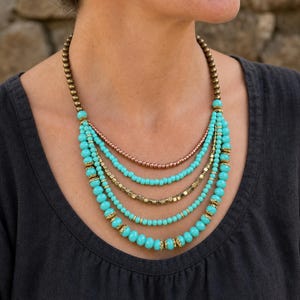 Gift ready presentation of Five strand turquoise copper and antique gold layered beaded statement necklace in an open jewelry box lined with natural ivory linen