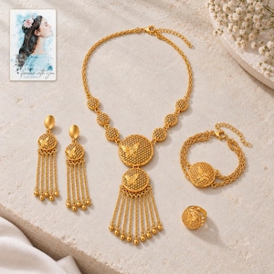 Puede incluir: Un conjunto de joyería en tono dorado que incluye collar, pendientes, pulsera y anillo. Cada pieza presenta un motivo circular con diseño de mariposa y textura de panal. El collar y los pendientes incluyen cadenas colgantes con pequeñas cuentas esféricas.