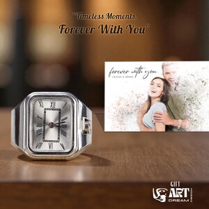 May include: A silver ring watch with a rectangular face, featuring Roman numeral hour markers and black hands. The watch is displayed next to a small print with the text "forever with you". The image also includes the text "Timeless Moments, Forever With You".