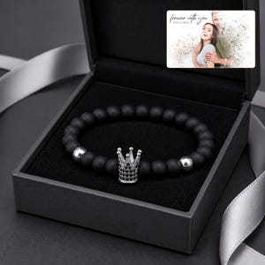 Puede incluir: Una pulsera de cuentas con esferas negras mate, dos esferas plateadas pulidas y un dije central de corona plateada incrustado con peque&ntilde;as piedras negras, presentada en una caja oscura con una tarjeta fotogr&aacute;fica que dice forever with you.