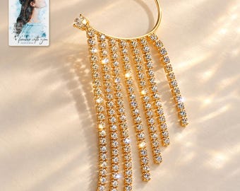 May include: A gold-tone ear cuff featuring a curved frame with two clear crystal studs and eight cascading fringe strands of clear crystals. A small rectangular card is included, displaying a watercolor illustration of a person and the text "forever with you".