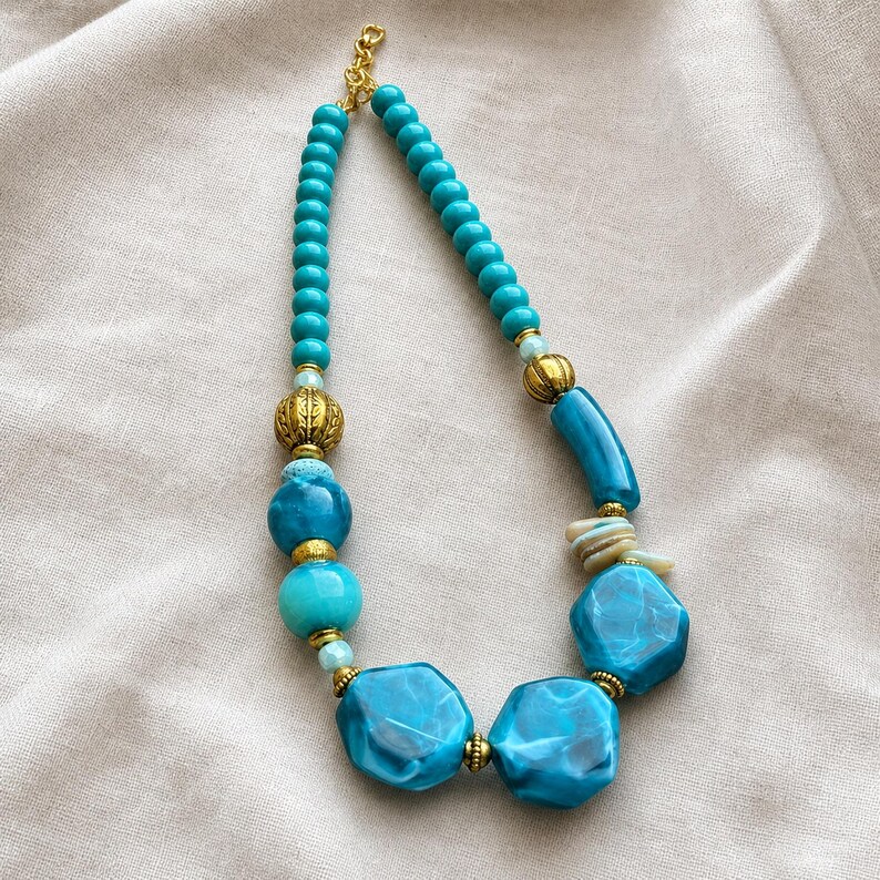 Blue and Clear Statement Beaded Necklace presented in an open jewelry gift box on natural linen