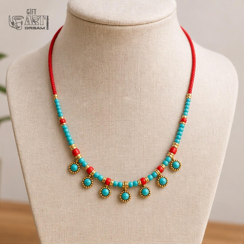 May include: A necklace featuring a red cord base accented with alternating turquoise and red beads, interspersed with gold-toned metal spacers. The lower section includes six dangling circular charms with turquoise centers and gold-toned beaded edges.