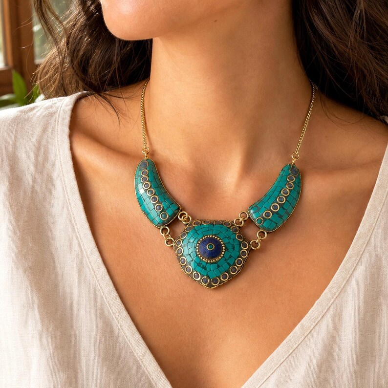 May include: A gold-tone necklace featuring a central triangular pendant and two curved side pieces, all inlaid with small turquoise-colored tiles. The center of the main pendant contains a circular dark blue stone surrounded by a gold-tone border.