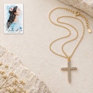 Complete gold-tone necklace arranged on ivory stone style, with an upright eleven-stone style cross, fine chain, spring-ring clasp and extension links. A personalized digital greeting card is shown alongside.