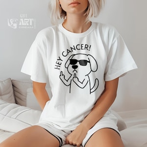 May include: White t-shirt with a black and white illustration of a dog wearing sunglasses and giving the middle finger. The text "Hey Cancer!" is above the dog.