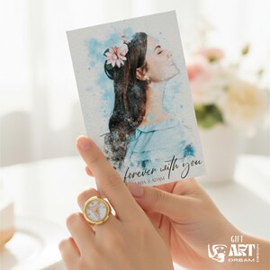 May include: A gold ring with a white face and a watercolour print card with a woman's portrait. The card has the text "forever with you" and is held in a person's hands. The ring is on the person's finger.