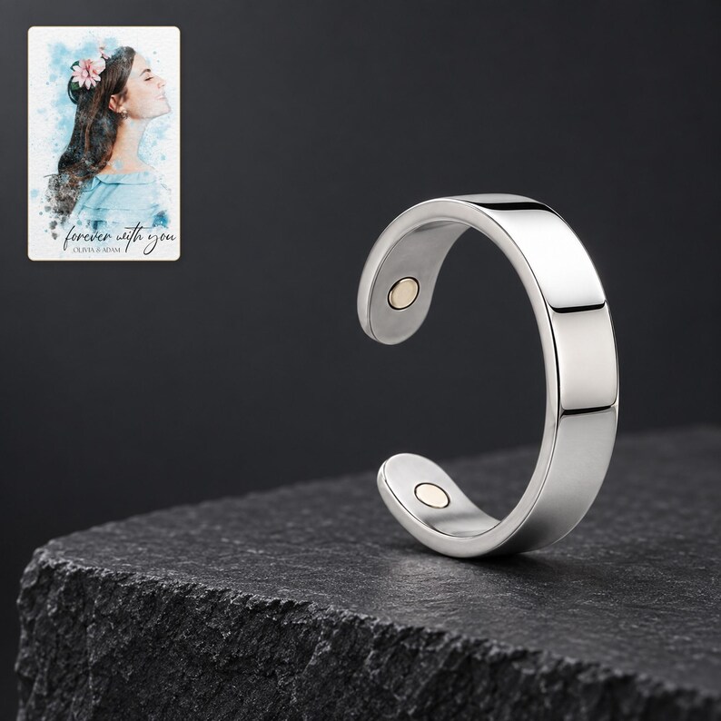 Reflective silver-tone open ring on a charcoal stone style plinth under soft studio lighting. A personalized digital greeting card is shown alongside.