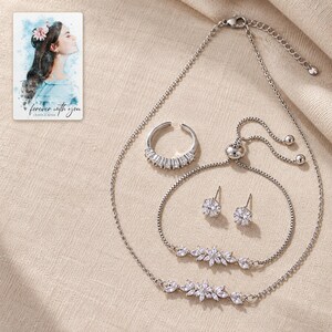 Matching silver-tone necklace, adjustable floral bracelet, open baguette ring and round stud pair arranged on oatmeal linen. A personalized digital greeting card is shown alongside.