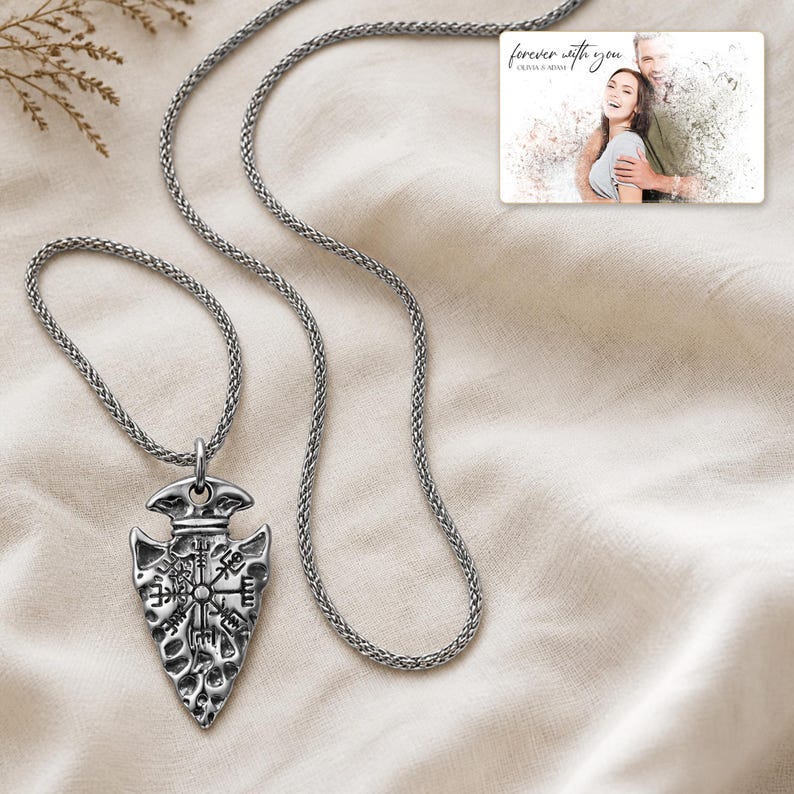 May include: A silver-toned arrowhead pendant necklace featuring an engraved Vegvisir symbol on a textured surface. The pendant hangs from a matching silver-toned chain. A rectangular card is included with the text "forever with you" and "OLIVIA & ADAM" above a photograph of a couple.