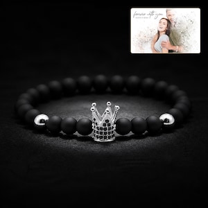 Puede incluir: Una pulsera de cuentas con esferas negras mate, dos esferas plateadas pulidas y un dije central de corona plateada incrustado con peque&ntilde;as piedras negras. Una foto muestra a una pareja con el texto forever with you.