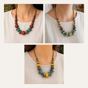 May include: Three necklaces featuring metallic gold-toned beads along the upper chain, accented with a central arrangement of textured, multi-colored beads in shades of red, turquoise, green, yellow, and brown, finished with flat disc-shaped beads.