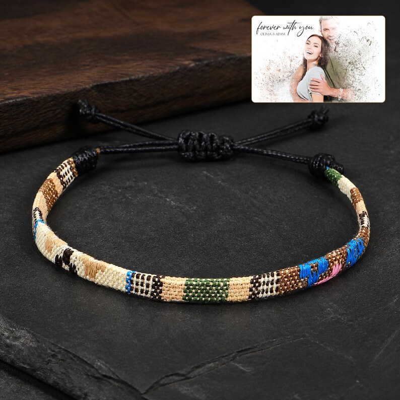 May include: A woven bracelet featuring a multicoloured geometric pattern in shades of tan, brown, green, and blue, with a black adjustable cord closure. The bracelet is displayed alongside a small rectangular card with the text forever with you.