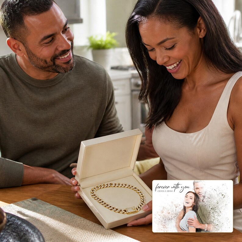 May include: A gold-toned cuban link chain necklace presented in an open cream-colored jewelry box. Beside the box is a rectangular card featuring a printed photograph of a couple with the text "forever with you" and "OLIVIA & ADAM" in script.
