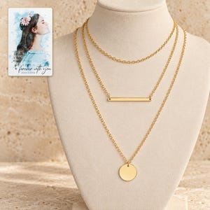 Gold-tone three-necklace set on an ivory display: plain short chain, narrow horizontal bar and smooth round disc, shown large against a pale surface. A personalized digital greeting card is shown alongside.