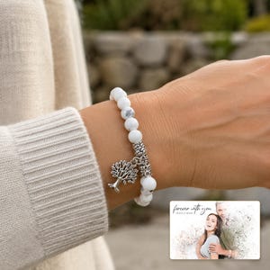 White and gray bead bracelet with silver-tone tree and hanging bead details, worn view. A personalized greeting-card example appears in the corner.