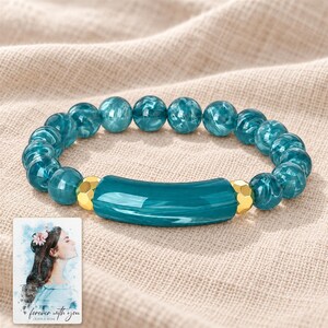 Peacock Tide Bar Bracelet arranged on soft ivory linen in a refined neutral flat lay. A personalized digital greeting card is shown alongside.
