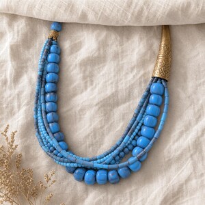 Gift ready presentation of Blue multi-strand statement necklace with asymmetric antique-gold caps in an open jewelry box lined with natural ivory linen