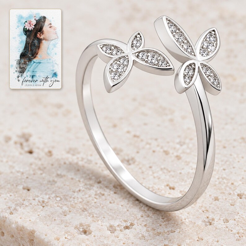 Double butterfly open ring with clear-accent wings displayed on warm ivory stone style. A personalized digital greeting card is shown alongside.