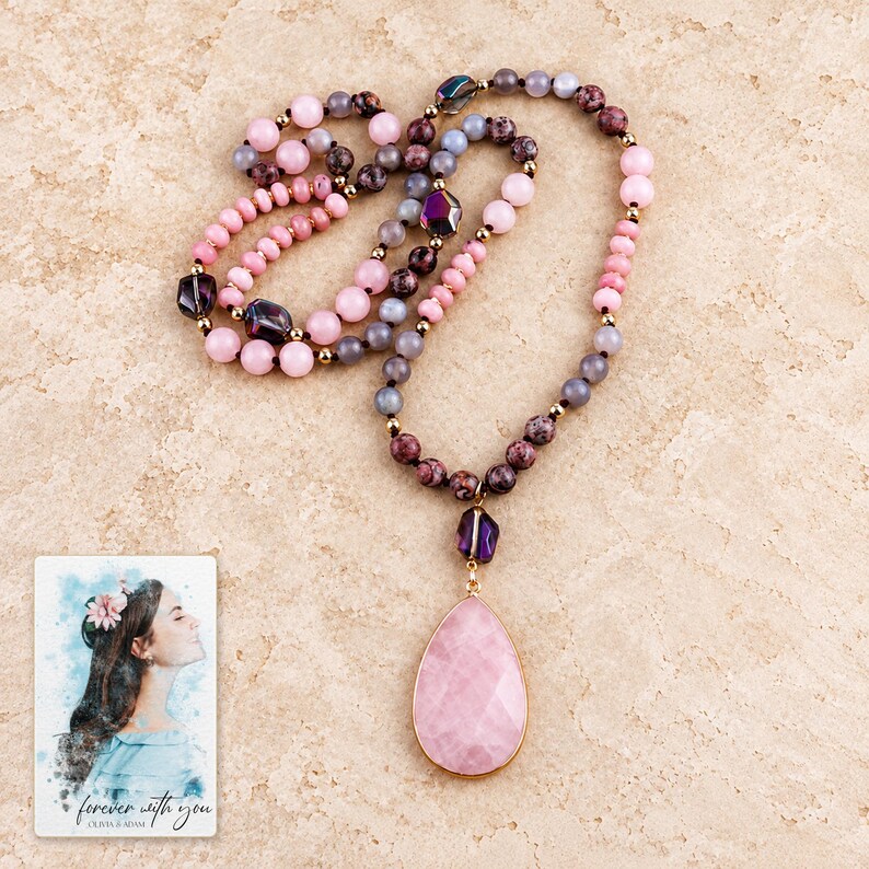 Pale-pink teardrop pendant necklace arranged on warm stone style, with purple faceted accents and mixed pink, smoky-grey and burgundy beads. A personalized digital greeting card is shown alongside.