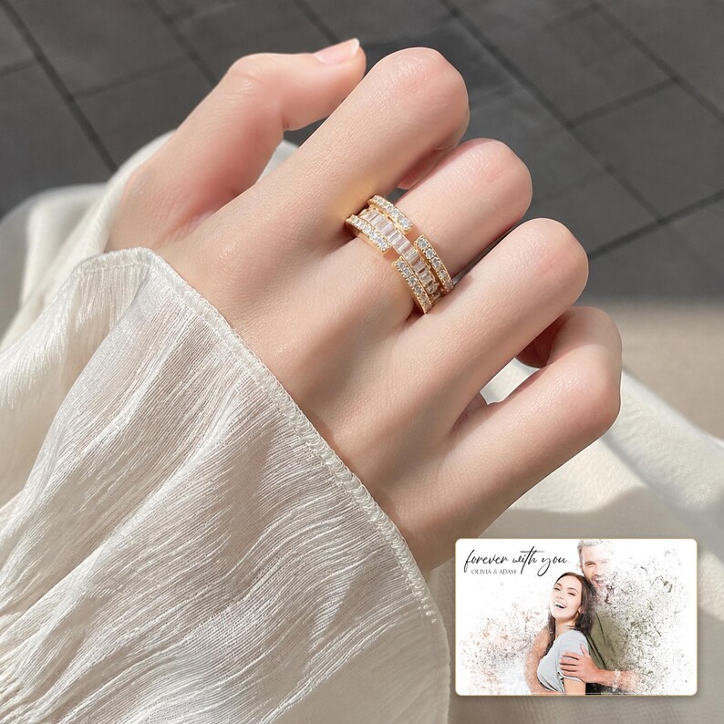 Gold-tone open ring with rows of clear accents, worn view. A personalized greeting-card example appears in the corner.