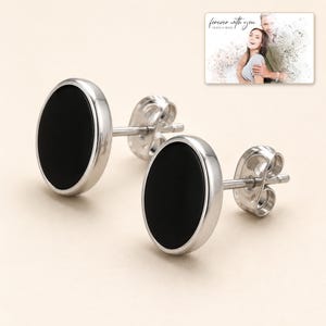 Black oval stud earrings with silver-tone edges, display view. A personalized greeting-card example appears in the corner.