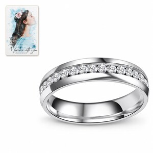 Single silver-tone clear accents band photographed on white, showing its continuous round shape and plain reflective interior. A personalized digital greeting card is shown alongside.