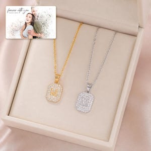 May include: Two necklaces with rectangular pendants featuring the letter M, one in gold tone and one in silver tone, both encrusted with clear stones. A small rectangular card is included with a photo of a couple and the text forever with you.