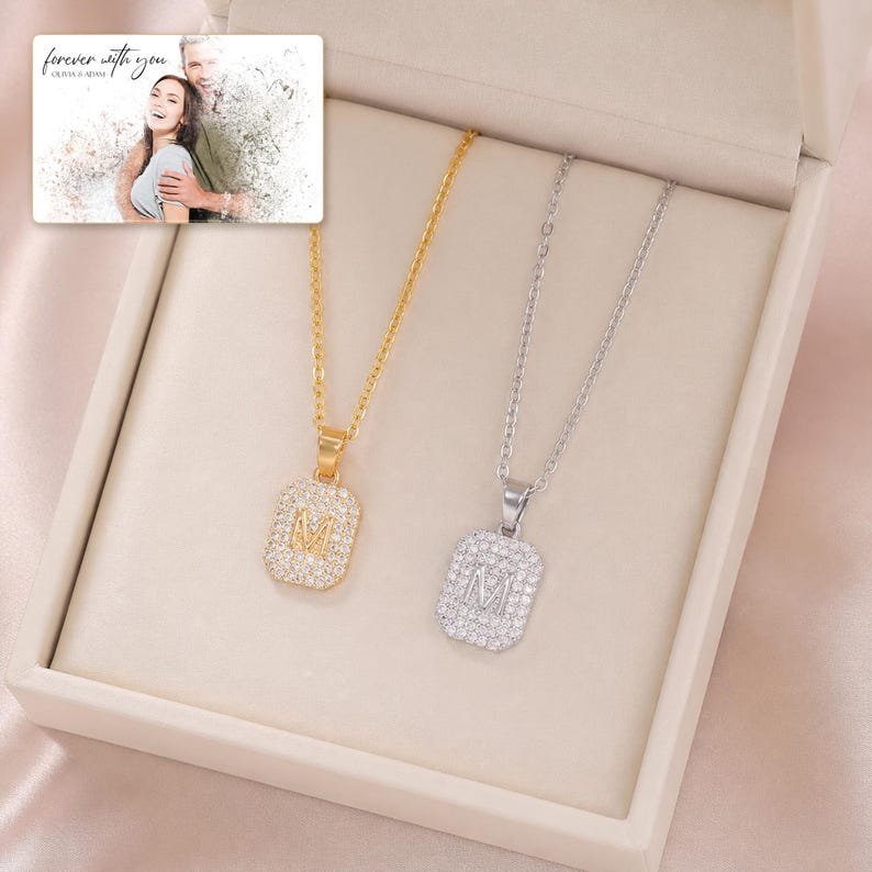May include: Two necklaces with rectangular pendants featuring the letter M, one in gold tone and one in silver tone, both encrusted with clear stones. A small rectangular card is included with a photo of a couple and the text forever with you.