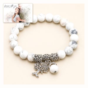White and gray bead bracelet with silver-tone tree and hanging bead details, catalog view. A personalized greeting-card example appears in the corner.