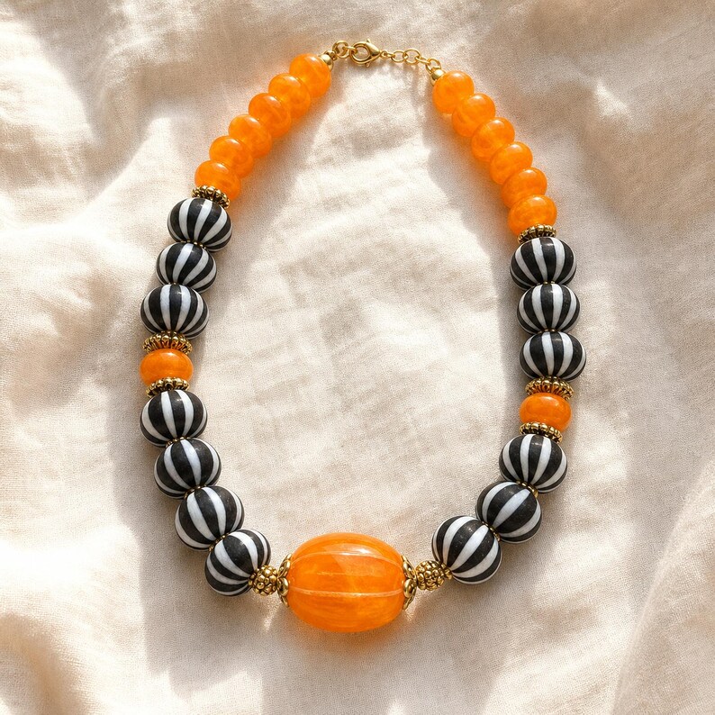 Gift ready presentation of Single-strand orange and black-and-white striped bead statement necklace with gold-tone spacers and a large orange oval center bead in an open jewelry box lined with natural ivory linen