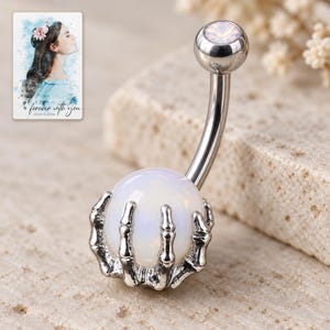 Macro view of articulated silver-tone skeletal fingers wrapping around the smooth milky-white ball. A personalized digital greeting card is shown alongside.