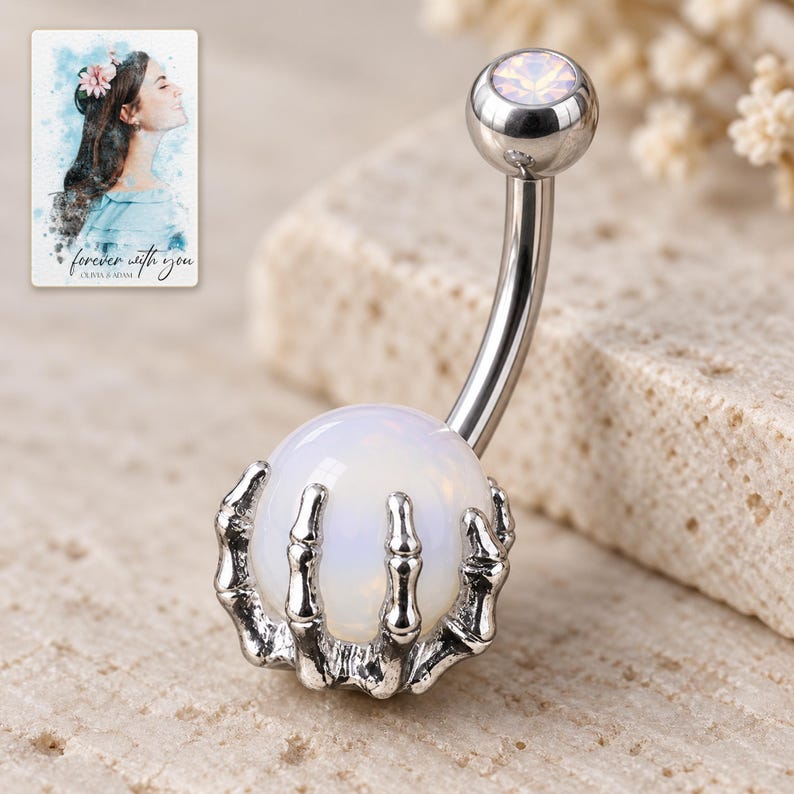 Macro view of articulated silver-tone skeletal fingers wrapping around the smooth milky-white ball. A personalized digital greeting card is shown alongside.