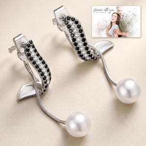 Silver-tone curved drop earrings with black accents and white round drops, close detail view. A personalized greeting-card example appears in the corner.