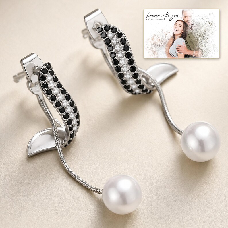 Silver-tone curved drop earrings with black accents and white round drops, close detail view. A personalized greeting-card example appears in the corner.