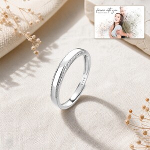 May include: A silver ring with a smooth center band and textured beaded edges, featuring an S925 hallmark stamp. In the upper corner, a rectangular card displays a photograph of a couple with the text "forever with you" and "OLIVIA & ADAM".