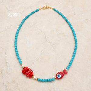 Turquoise Beaded Fish Evil Eye Necklace presented in an open jewelry gift box on natural linen
