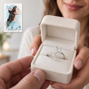 Adult woman receiving an open ivory jewelry box holding the clear-accent double butterfly ring. A personalized digital greeting card is shown alongside.