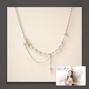 Silver-tone layered necklace with pale beads and pointed star charms, dark-bordered product view. A personalized greeting-card example appears in the corner.