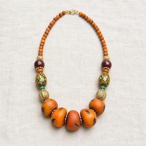 Gift ready presentation of Burnt orange statement beaded necklace with mosaic and antique gold accent beads in an open jewelry box lined with natural ivory linen