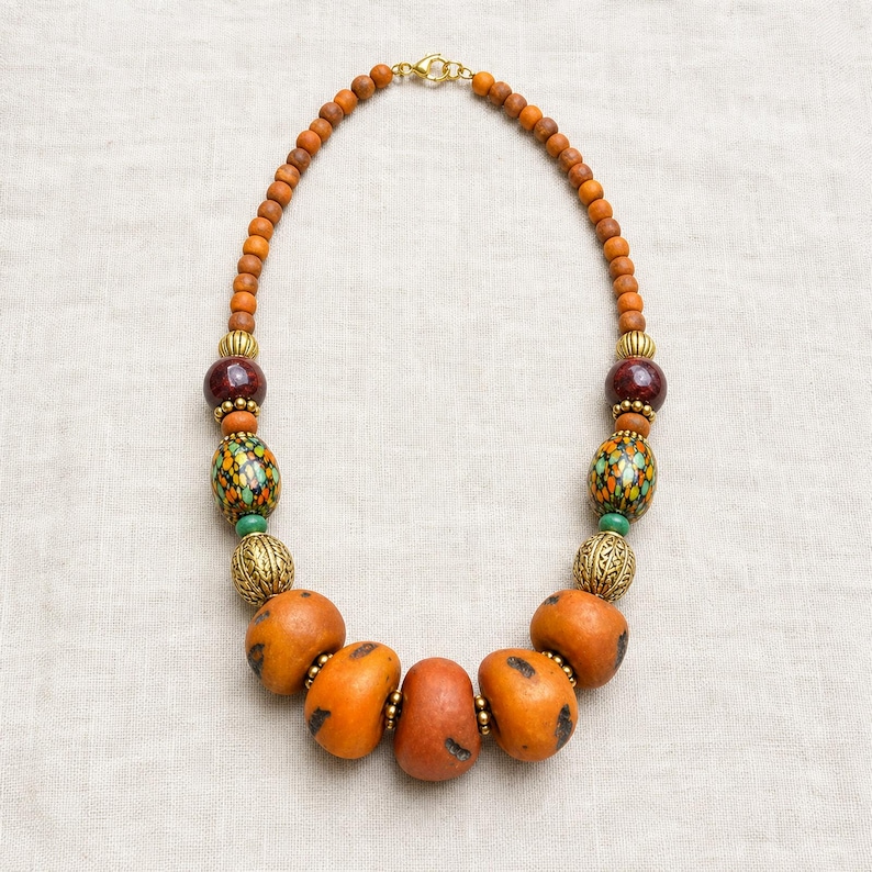 Gift ready presentation of Burnt orange statement beaded necklace with mosaic and antique gold accent beads in an open jewelry box lined with natural ivory linen