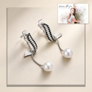 Silver-tone curved drop earrings with black accents and white round drops, framed product view. A personalized greeting-card example appears in the corner.