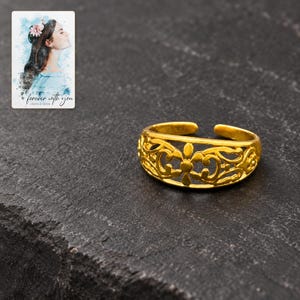 Golden Bloom Filigree Ring styled against a dark luxury surface with the exact product finish clearly visible. A personalized digital greeting card is shown alongside.