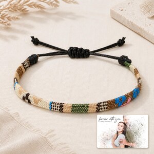 May include: A woven bracelet featuring a multi-coloured geometric pattern in shades of tan, brown, green, and blue, with a black adjustable cord closure. A small rectangular card displays the text "forever with you" above a photo of a couple.