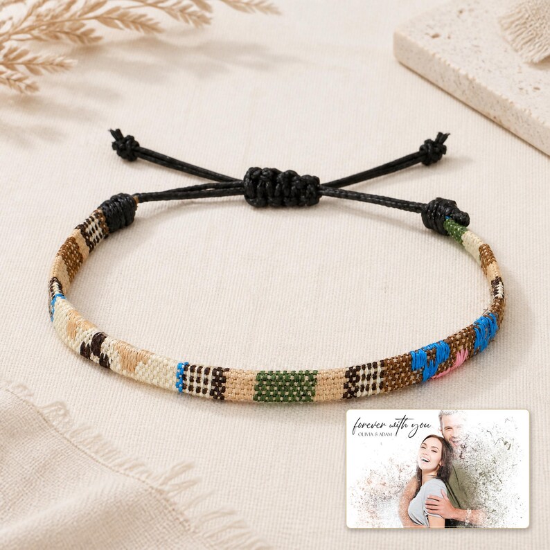 May include: A woven bracelet featuring a multi-coloured geometric pattern in shades of tan, brown, green, and blue, with a black adjustable cord closure. A small rectangular card displays the text "forever with you" above a photo of a couple.